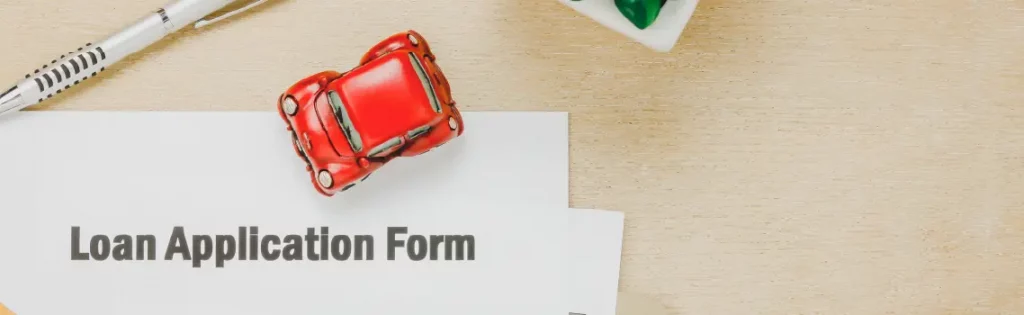 Loan application form on a desk with a miniature red car and pen, representing the process of applying for a loan.